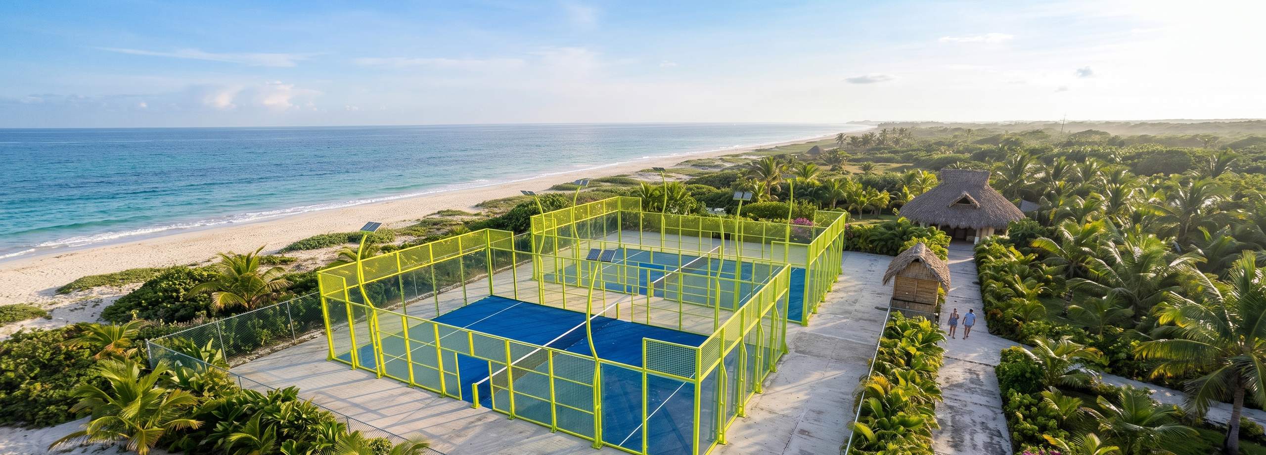 Dos canchas de pádel Anti Hurricane de Orion XSport en un club costero al amanecer, con estructura en amarillo flúor, césped azul y columnas de celosía de refuerzo estructural, y el mar al fondo. Fabricación directa de fábrica.