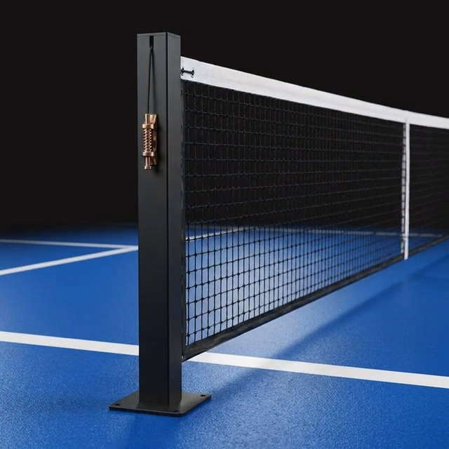 Conjunto de postes fixos Post Fixed da Orion XSport montado em uma quadra de pickleball, com a rede colocada, o tensor de parafuso sem-fim à vista e a placa-base aparafusada ao piso. Fabricação direto da fábrica.
